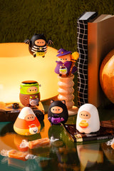 Halloween-themed Tayto Potato figures on a reflective surface with a warm light source. Tayto Trick-or-Treats as Candy Corn Tayto, Franken-Tayto, Spooky Black Cat Tayto, Skeleton Bat Tayto, Warlock Tayto, Ghost Tayto.